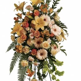 Tall standing floral spray with yellow lilies, peach roses, and pale gerberas