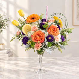 Colorful flower arrangement in a clear glass vase with a striped candle and lemon slice