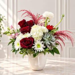 Red roses and white blooms in a white face vase with pink accents