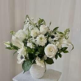 White floral arrangement in a white vase with roses and calla lilies