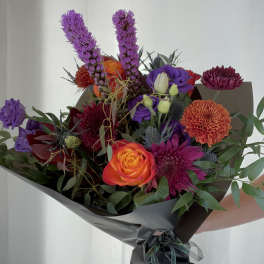 Mixed bouquet with orange and purple flowers wrapped in dark paper