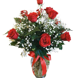 Red roses arranged in a glass vase with a red ribbon