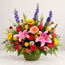 Colorful mixed flower arrangement in a green bowl vase with lilies and roses