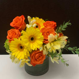 Orange roses and yellow gerbera daisies in a dark vase