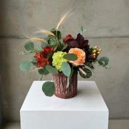 Mixed bouquet in a textured brown vase with peach, red, and green blooms