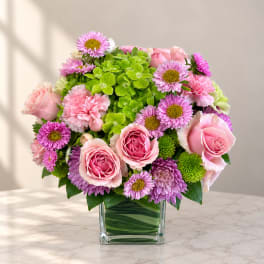 Pink roses and purple daisies in a clear square vase