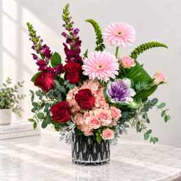 Mixed bouquet in a glass vase with roses, gerbera daisies, and purple blooms