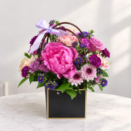 Pink and purple mixed flower arrangement in a black box with a lavender ribbon