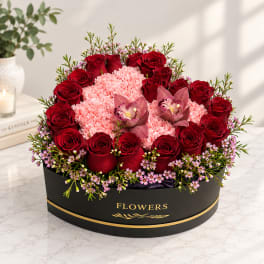 Round box arrangement of red roses, pink carnations, and orchids