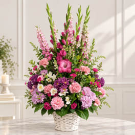 Tall pink and purple flower arrangement in a white basket vase