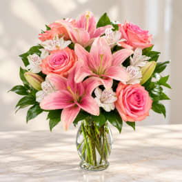 Pink lilies and roses arranged in a clear glass vase