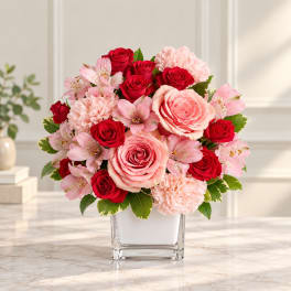 Pink and red roses with carnations and alstroemeria in a square glass vase