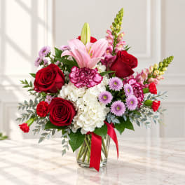 Mixed bouquet of red roses, pink lilies, and white hydrangeas in a glass vase