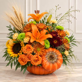 Orange floral arrangement in a pumpkin container with lilies and roses