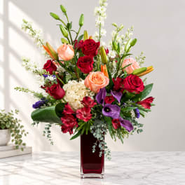 Mixed bouquet of roses, lilies, and purple calla lilies in a tall red vase