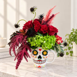 Red roses and bright green hydrangeas in a decorated skull mug