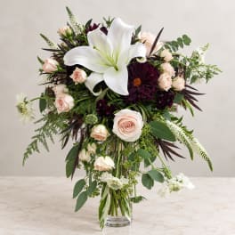 Wedding bouquet with white lilies, blush roses, and dark burgundy blooms in a glass vase