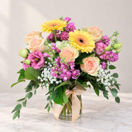 Bouquet of peach roses, yellow gerbera daisies, and pink flowers in a glass vase