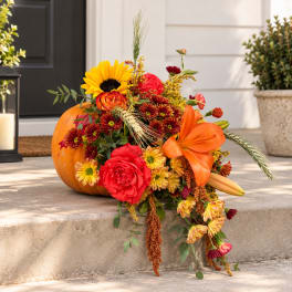 Autumn bouquet with sunflowers, roses, lilies, and chrysanthemums beside a pumpkin
