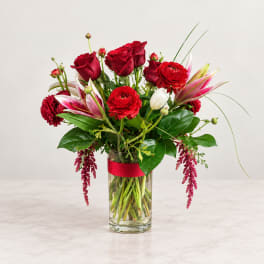 Red roses and lilies arranged in a clear glass vase with a red ribbon