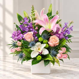 Pink lilies and roses in a white square vase with purple blooms