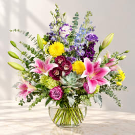 Mixed bouquet in a clear glass vase with lilies, roses, and purple blooms