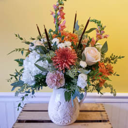 Mixed floral arrangement in a white ceramic pitcher vase
