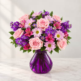Pink roses and purple mixed flowers in a purple glass vase