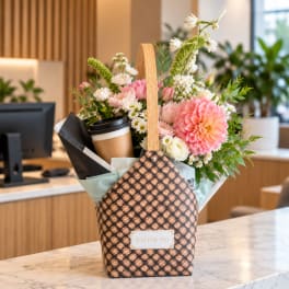 Pink and white flower arrangement in a woven gift basket with a coffee cup