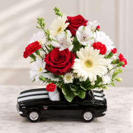 Red roses and white daisies arranged in a black car-shaped container