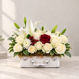 White lilies and roses arranged in a white suitcase-style container