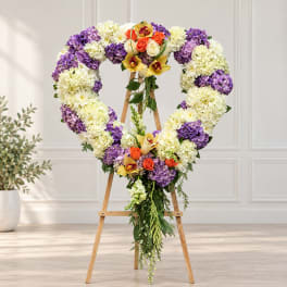 Heart-shaped floral wreath on a wooden easel with purple, white, and orange flowers