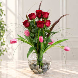 Red roses and pink tulips in a round glass vase with stones