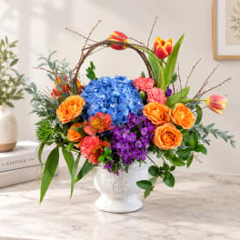 Colorful floral arrangement in a white pedestal vase with a twig arch