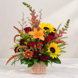 Mixed bouquet with sunflowers, roses, lilies, and snapdragons in a patterned vase