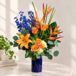 Orange roses, lilies, and blue delphinium in a cobalt vase