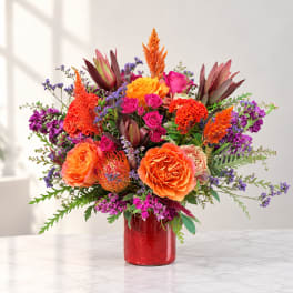 Bright mixed bouquet of orange, pink, and purple flowers in a red vase