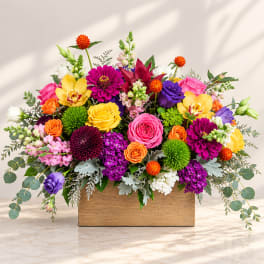 Bright mixed flower arrangement in a wooden box with roses and orchids