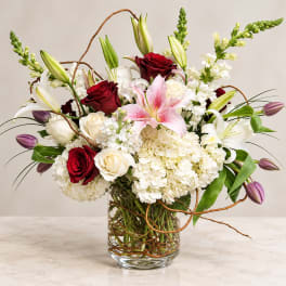Bouquet of red and white roses, lilies, and hydrangeas in a glass vase