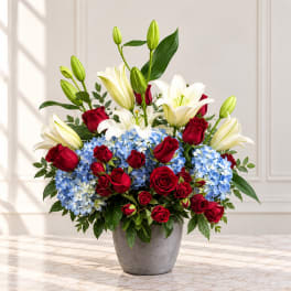 Red roses, white lilies, and blue hydrangeas in a gray vase