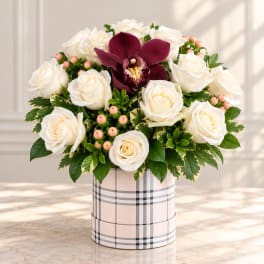White roses and a burgundy orchid in a plaid hatbox arrangement