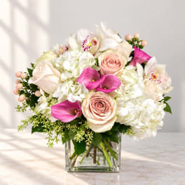 Bouquet of white hydrangeas, blush roses, and pink calla lilies in a glass vase