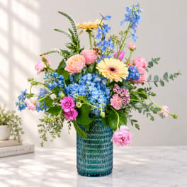 Mixed bouquet of pink, blue, and yellow flowers in a blue glass vase