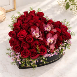 Red roses and pink orchids arranged in a black heart-shaped box
