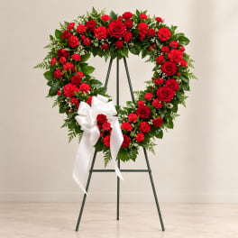 Heart-shaped red floral wreath on an easel with a white bow
