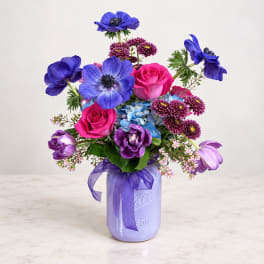 Bouquet of blue, pink, and purple flowers in a lavender mason jar