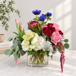 Mixed bouquet in a clear square vase with pink, red, white, and blue flowers