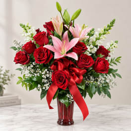 Red roses and pink lilies in a red glass vase with a ribbon