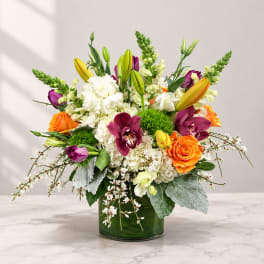 Colorful bouquet in a green glass vase with lilies, roses, orchids, and white blooms