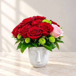 Red roses and a pink rose in a white face vase